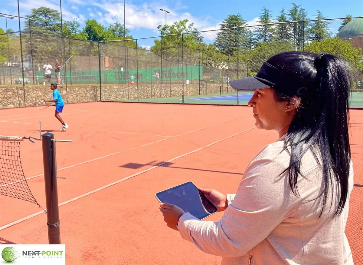 A NextPoint coach with an iPad watching a junior train on the clay court