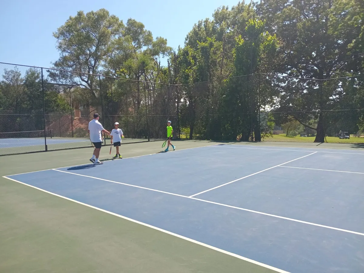 A NextPoint coach on court with two juniors during a squad session