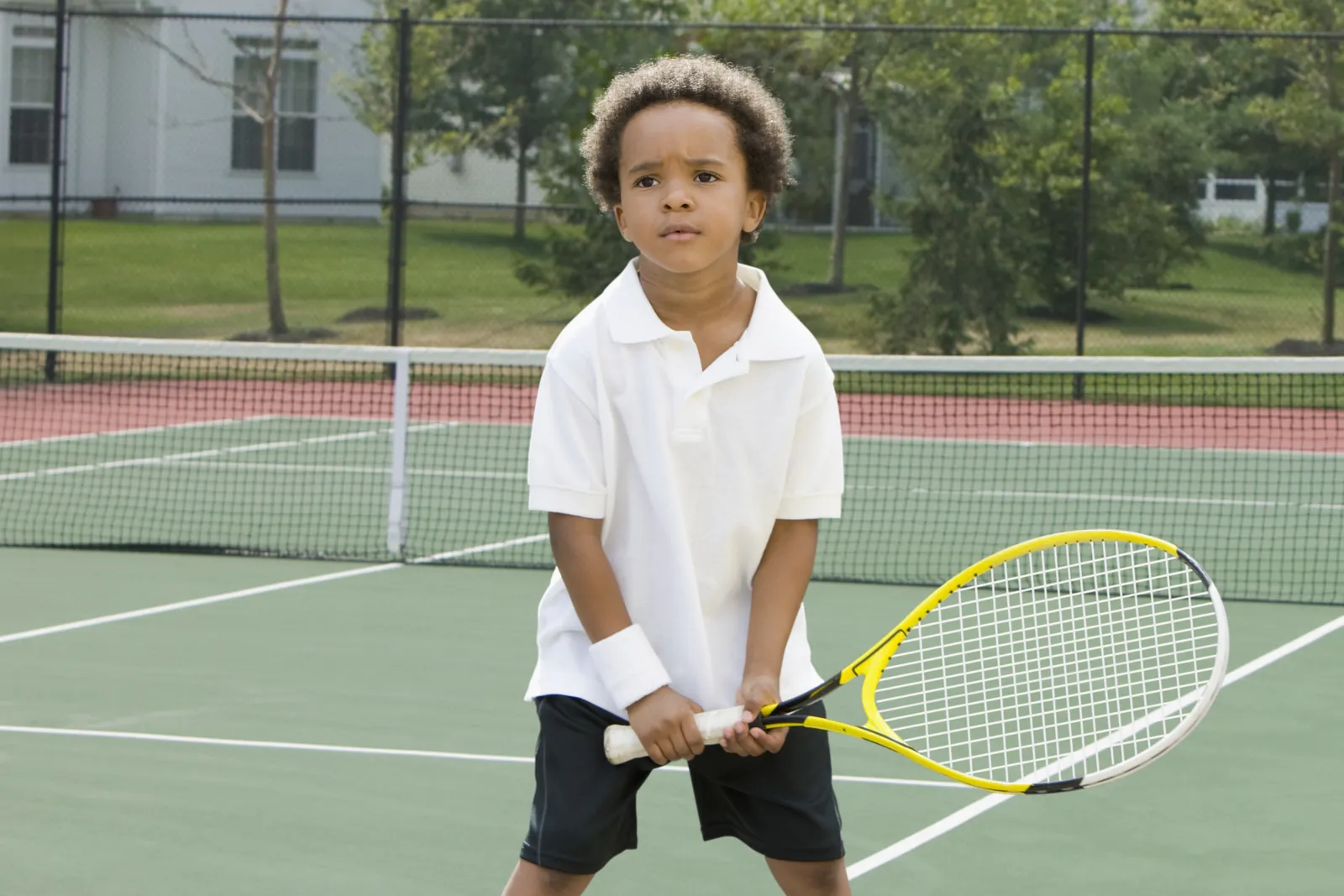 A young player waits at the ready, racquet in both hands — programs start here