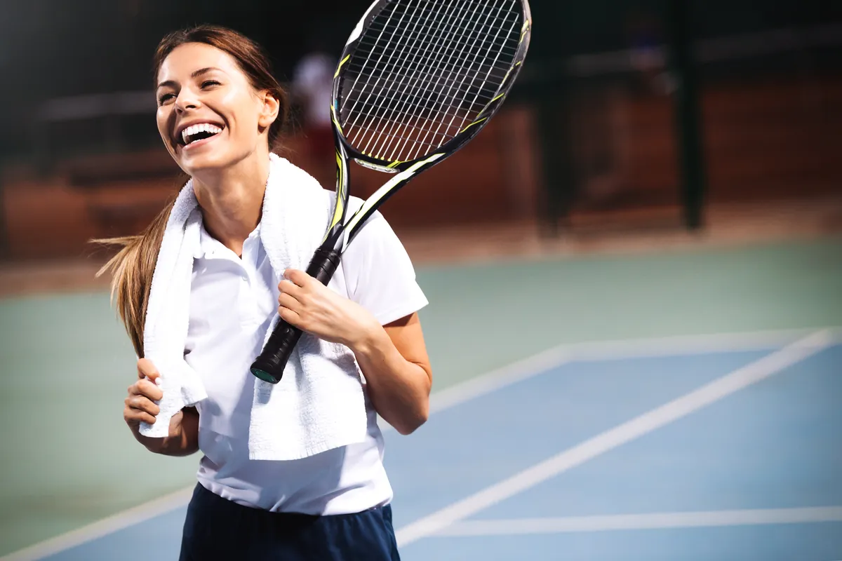 A player grinning mid-session, towel around her neck — Cardio Tennis energy